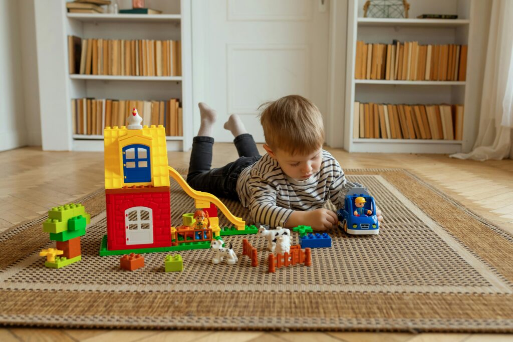 misja i wizja Young child playing with colorful building blocks and toy car on a woven carpet in a home setting.