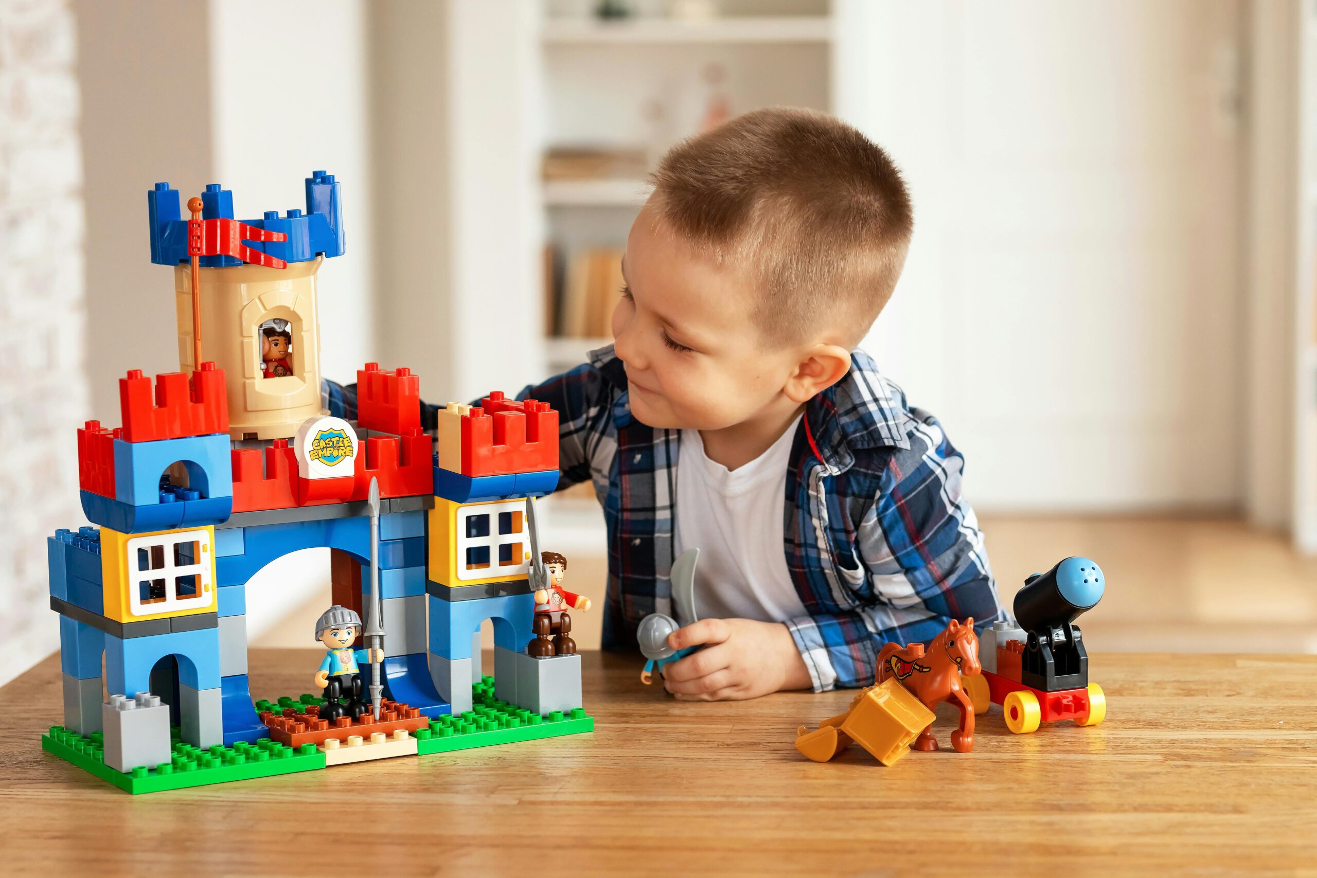 warsztaty, Young boy playing creatively with toy castle and figurines indoors, fostering imagination.