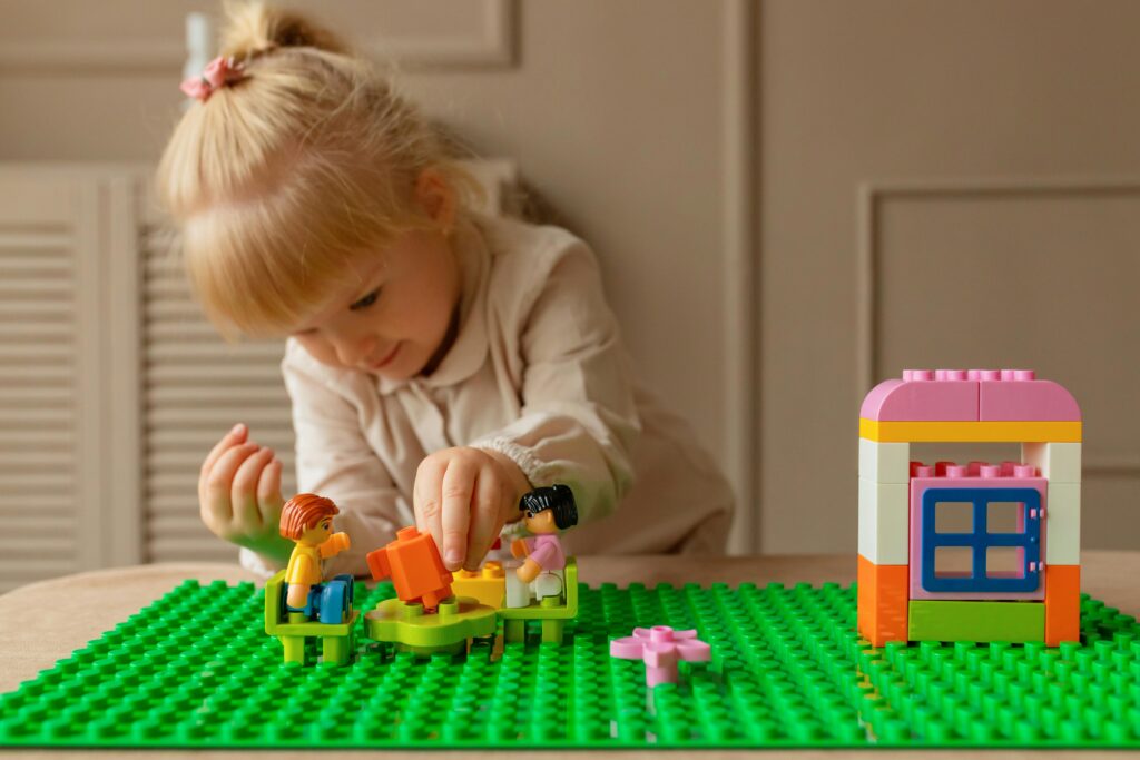 Play&Brain, A young girl engaging creatively with colorful plastic building blocks on a table indoors.