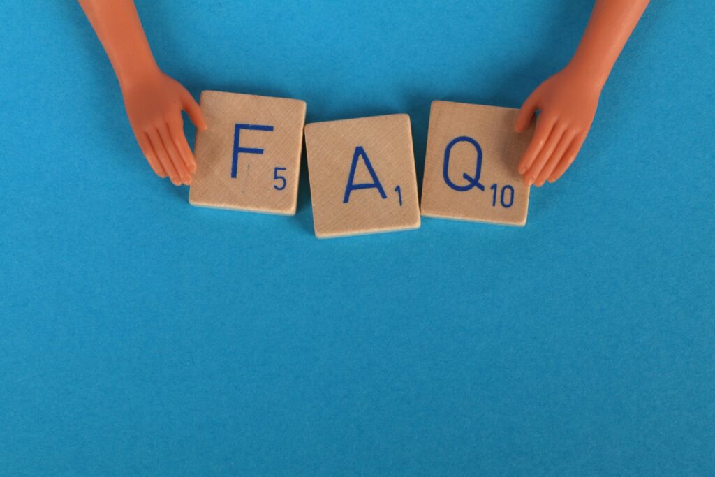 FAQ, Flat lay of scrabble tiles spelling 'FAQ' with toy hands on a blue background, creating a conceptual image.